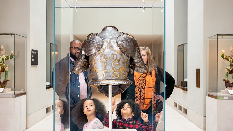 A young family group looking at a bust of armour while enjoying a day out at The Burrell Collection