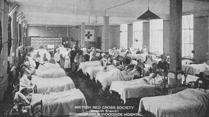 Black and white photo of a hospital ward at Springburn and Woodside hospital showing multiple beds side by side in the ward with nurses and doctors standing around.