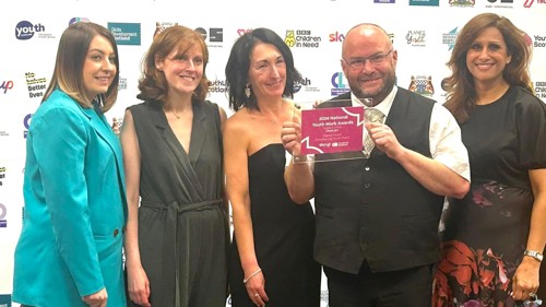 A group of five people at an awards ceremony. One is holding up a square glass award