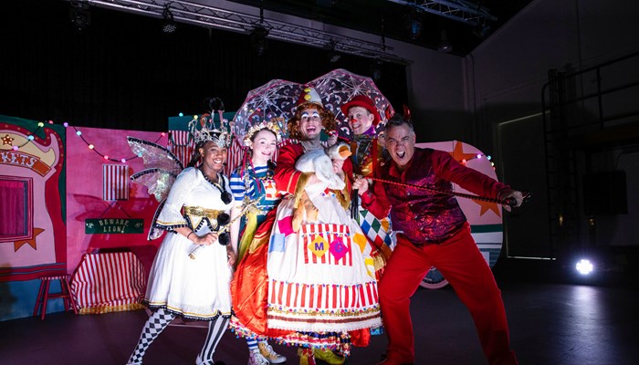 Pantomime performers in colourful costume pose in front of a circus-themed set 