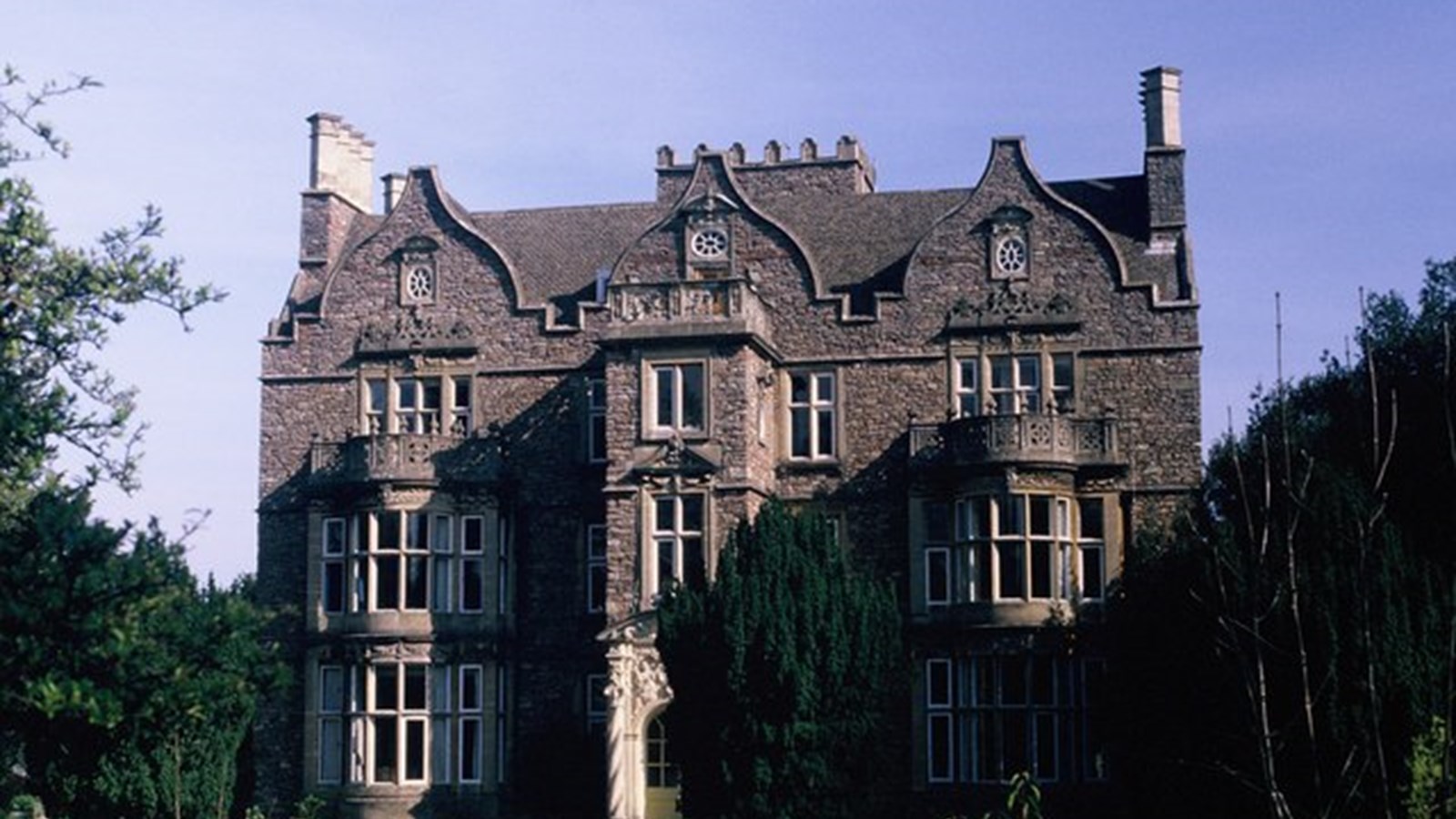 a photograph of a medium sized country house. It has 3 storeys, a protruding room on the front elevation and single bay windows on either side
