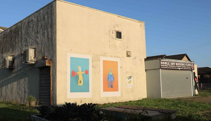 A building has two large posters showing community made clay sculptures. 