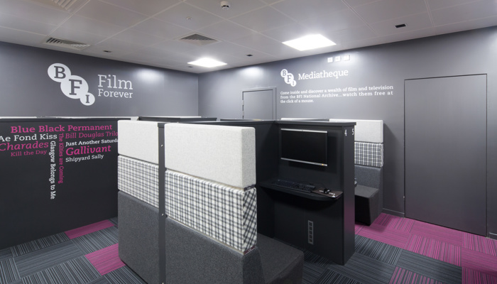 Grey and purple designed mediateque with a booth which has a table, bench and a TV. There is writing on the wall which reads 'BFI Film Forever'