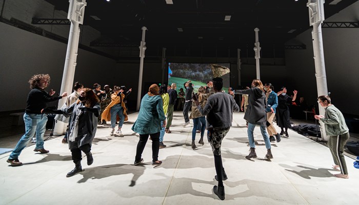 A large group of people dance together in a vast gallery space