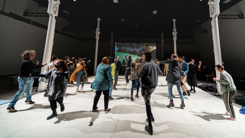 A large group of people dance together in a vast gallery space