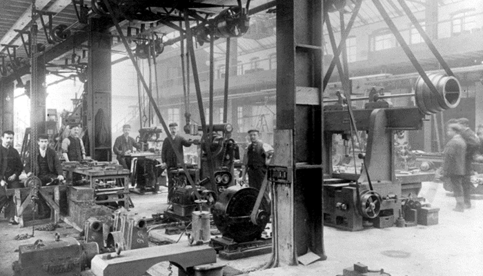 A black and white photocopy of workers in a warehouse operating heavy machinery. 