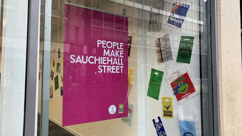 An image of a pink poster in a high-street window. The poster says 'people make Sauchiehall Street' in capital letters and white text.