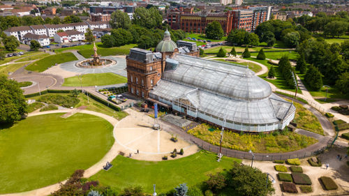 Aerial shot of the People's Palace and Winter Garden in Glasgow. A sandstone museum building with large glasshouse to the rear, situated in a large park area
