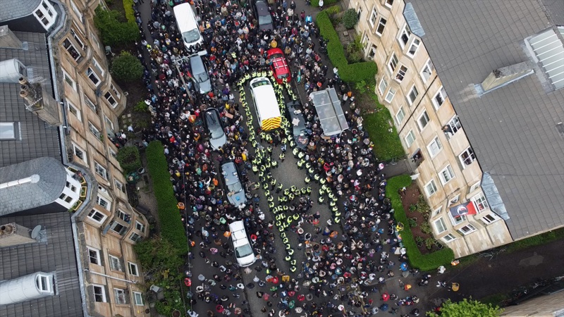 Aerial view of a large crowd gathered on Kenmure Street in Glasgow, surrounding a police van while officers form lines through the street between rows of tenement buildings.