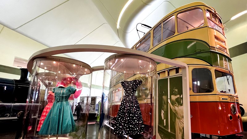 Photograph showing a selection of vintage dresses and a tram, both of which would have been used to go out dancing