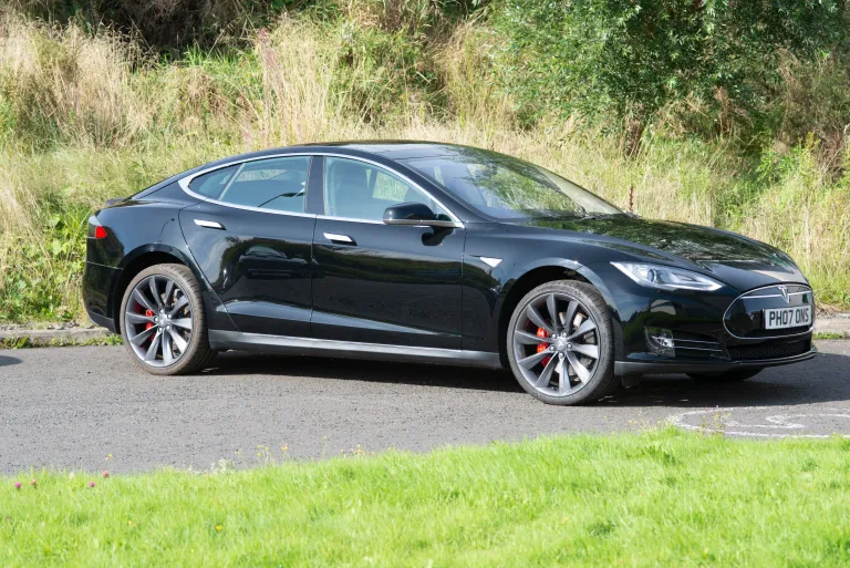 photo of a black Tesla electric car on a road among grass.
