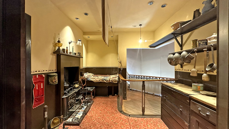 Photograph shows a recreation and display of a bed in a kitchen of what a single end tenement flat would have been like