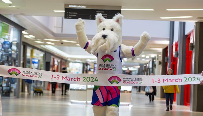 A Scottish Terrier mascot runs through a finish line promoting the 2024 World Athletics Indoor Championships in Glasgow