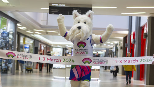 A Scottish Terrier mascot runs through a finish line promoting the 2024 World Athletics Indoor Championships in Glasgow