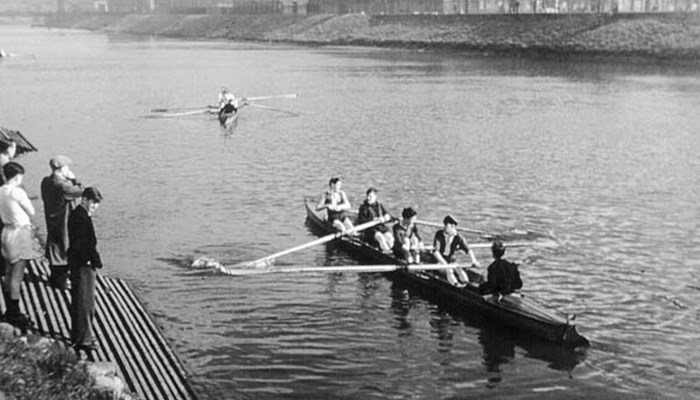 A black and white photo of people rowing on the river Clyde and other people watching from the sides.