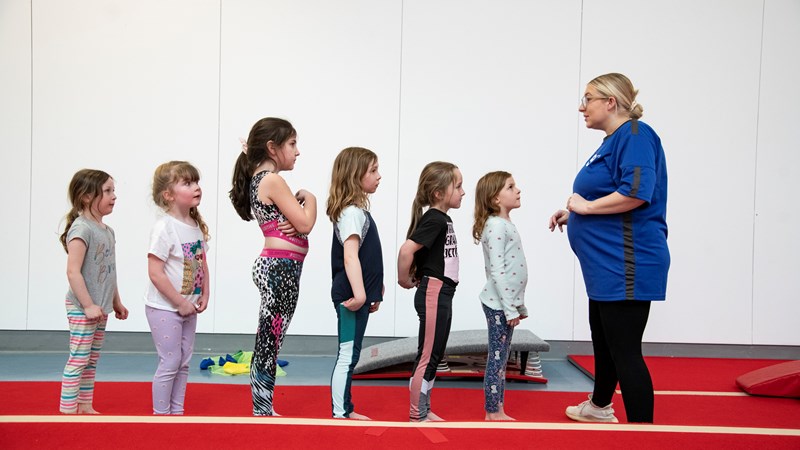 A group of children lined up in front of a gymnastics instructor during a class