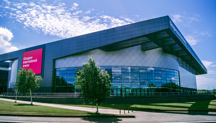 Glasgow International Arena exterior with curved glass frontage and signage beneath a bright sunlit sky.