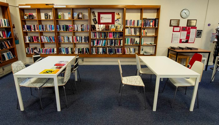 Two white rectangular tables in front of brown wooden bookshelves filled with books. 