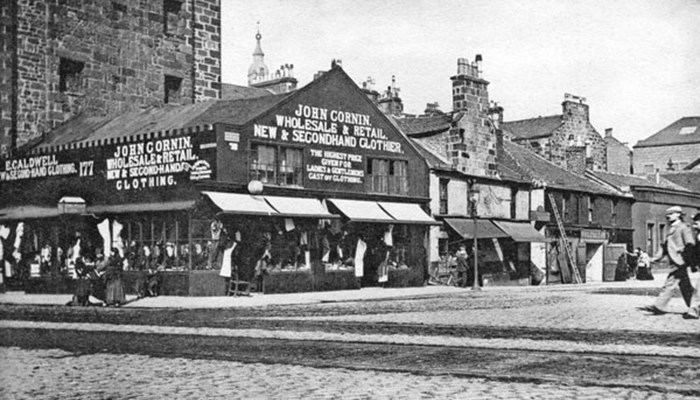 A photo of a black and white postcard showing shops and a theatre on a Glasgow street and pedestrians walking around.