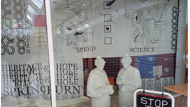 An exhibition of sculpture and textiles is pictured through a shopfront window