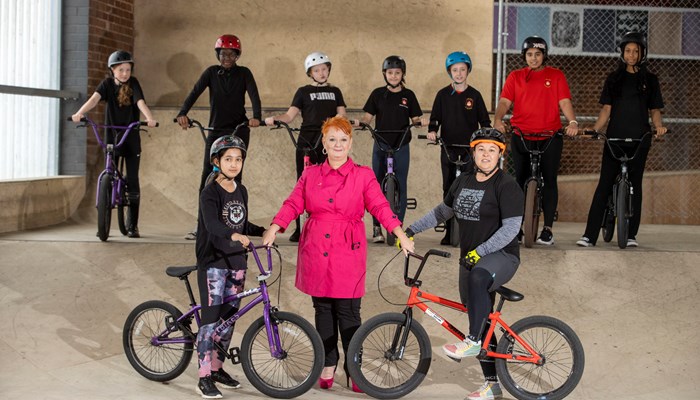 Young women dressed for cycling on bikes with woman councillor on indoor ramps.