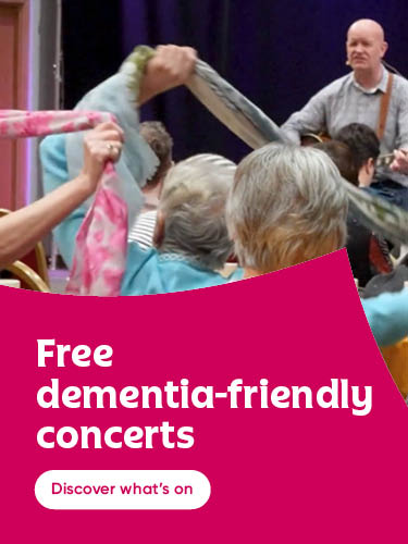 People taking part in a dementia-friendly concert, moving colourful scarves during a live music performance.