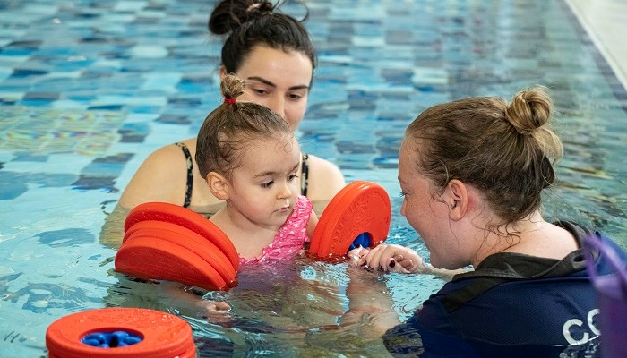 A swimming coach helping a parent put armbands on a child