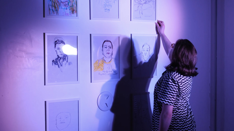 A person arranges portraits on a wall for an exhibition. 