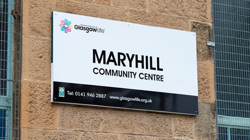 black and white sign that says maryhill community centre. it is attached to a brick wall outside the building