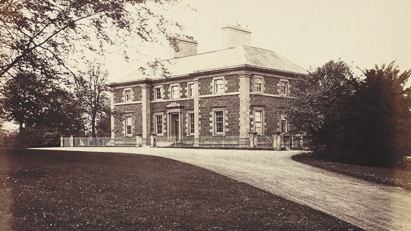 A black and white photo of Cathkin House which has white railings around it, a path leading up to the entrance plus a large lawn with mature trees and shrubs.