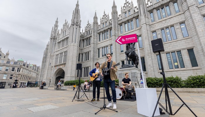 Aberdeen band Pages perform on guitars and a drumkit in front of the granite Aberdeen City Council offices
