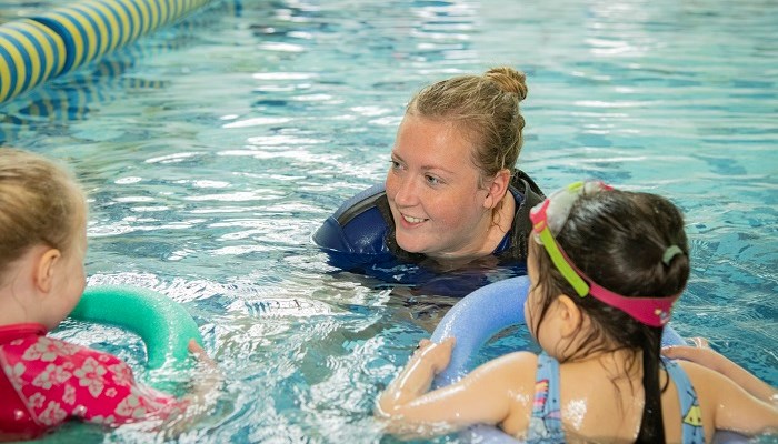 A swimming coach talking to two young children while in the pool