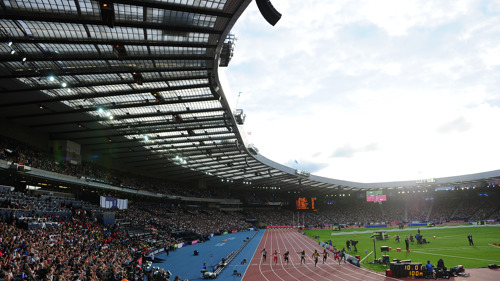 Athletics taking place at Hampden Park during the Glasgow 2014 Commonwealth Games. Athletes are running over the finish line while thousands of people watch from the stands.