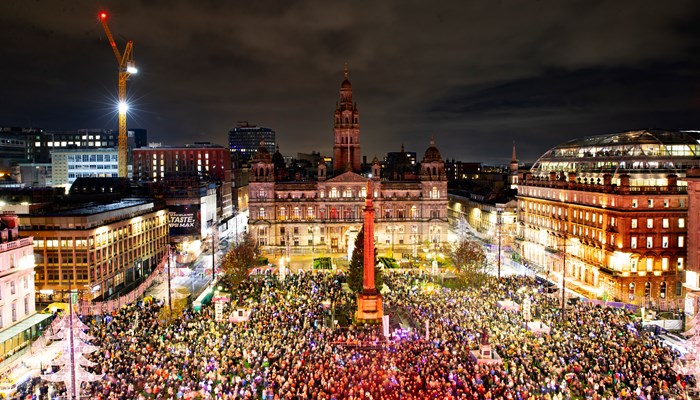 An aerial shot shows thousands of people gathered in a large civic square with a large monument in the middle and festive lighting round the perimeter