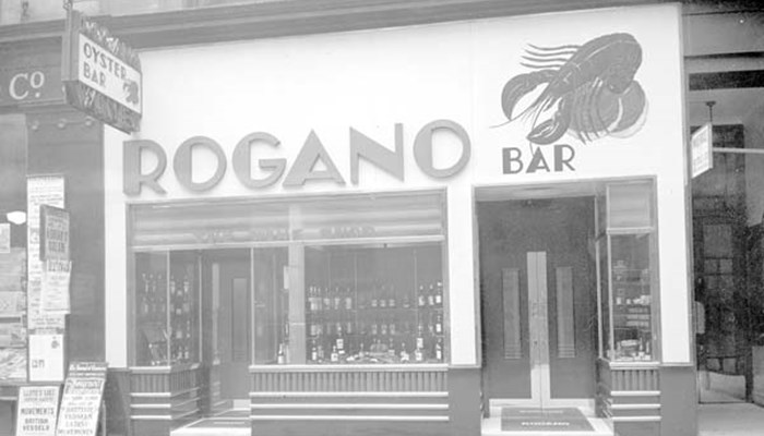 A black and white photo of Rogano's restaurant bar in Glasgow which has a shellfish as part of it's signage and lots of bottles of wine in the windows.