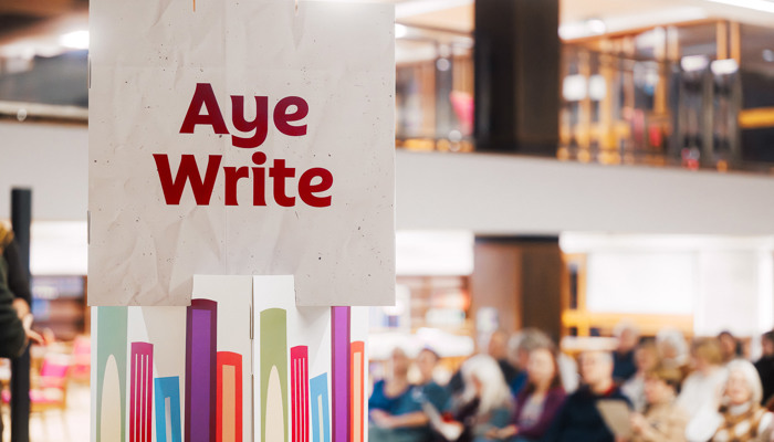 A sign for 'Aye Write' is visible next to an audience at a book festival event