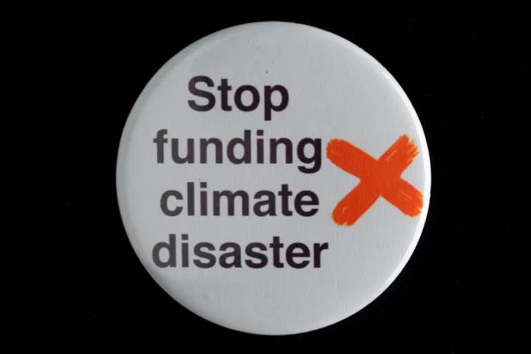 photo of a plastic badge bearing the words "stop funding climate disaster"