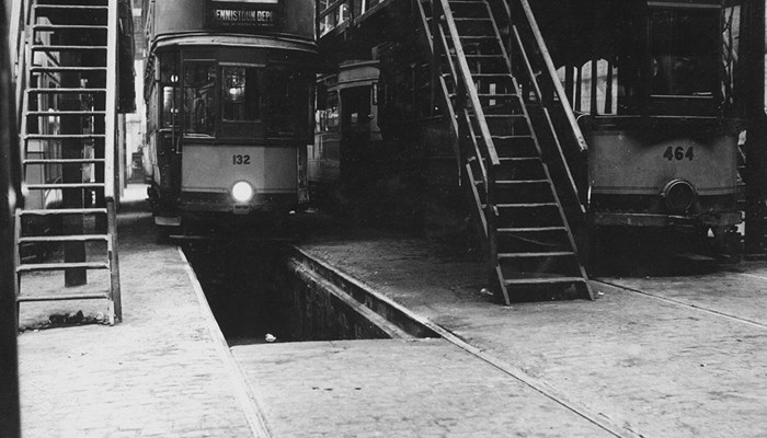 A black and white photograph of trams in a depot with ladders at each side and space underneath for maintenance checks.