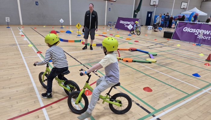 Young children cycling around an indoor obstacle course.