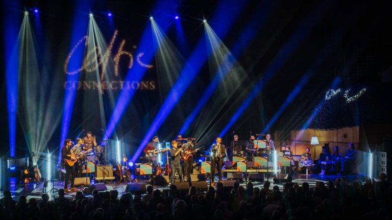 A large band performs under dramatic blue and white lights, with the Celtic Connections logo projected in the background.