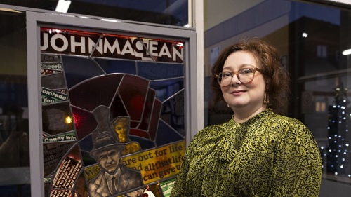 A person wearing glasses standing next to a stained glass window display in a frame in a library
