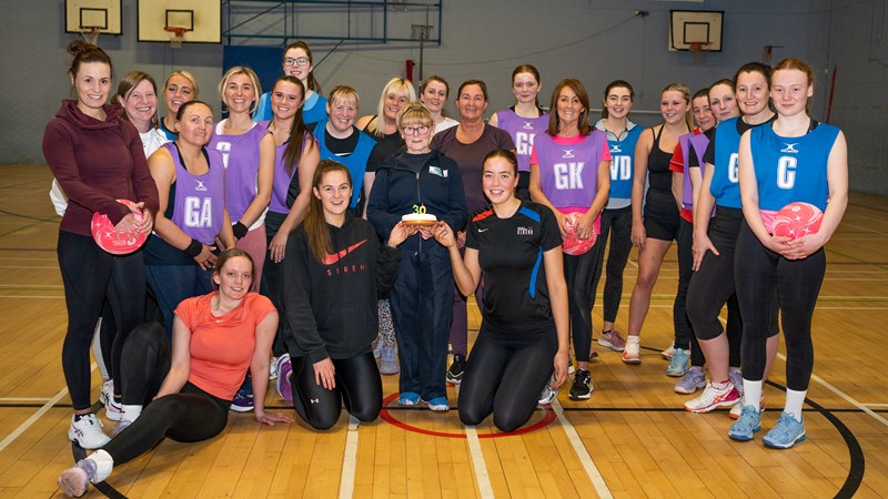 A netball team standing together and standing while some of them hold netballs
