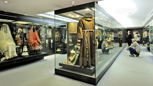 Photograph showing glass cabinets housing displays of Religious clothing.