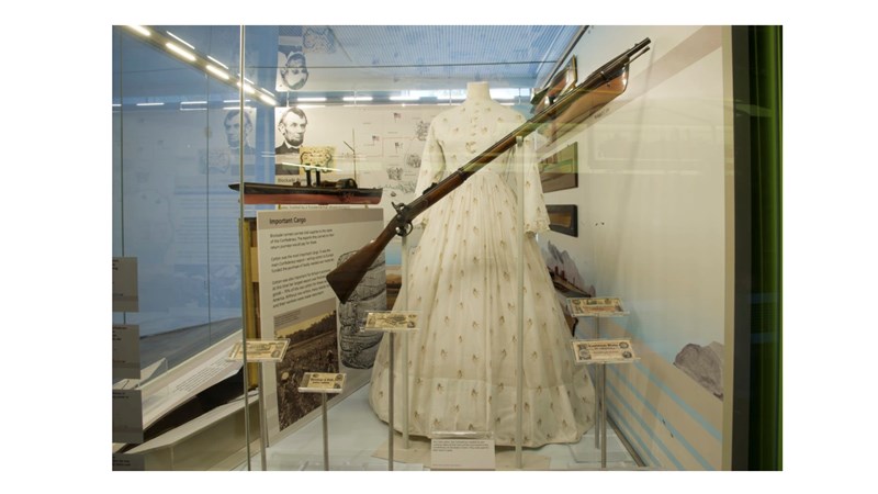 an image showing a musket and a long white dress in a display case