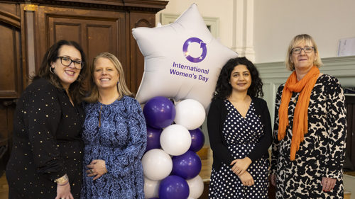A group of four people smiling for a photo next to a star shaped balloon with text International Women's Day