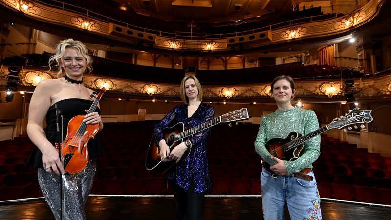 Three musicians standing on stage at a theatre holding their instruments