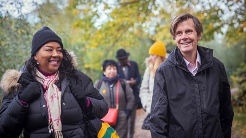 A group of five people enjoying a winter walk in a forested park. They are smiling and wearing winter coats and warm hats