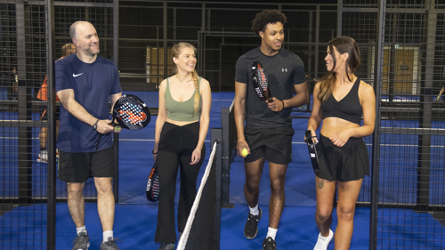 Four people wearing sports clothing are entering an indoor padel court about to start a game of doubles