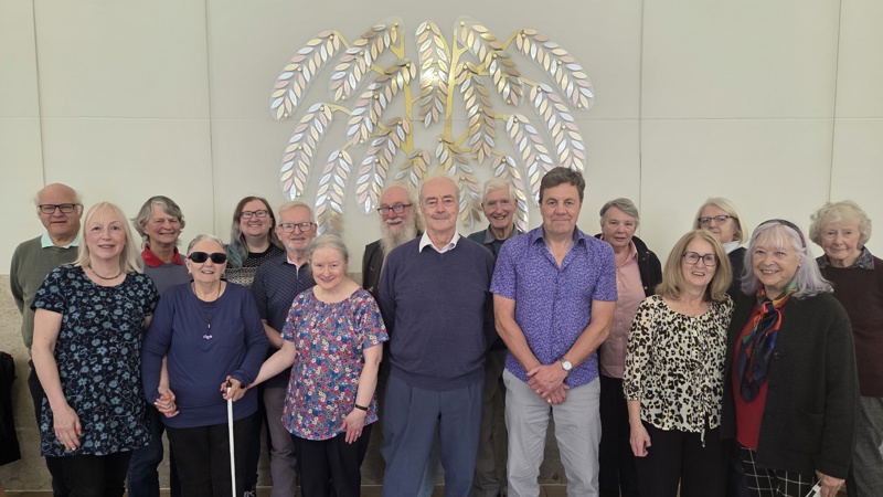A group of people gathered in front of a piece of metal wall art in the shape of a tree