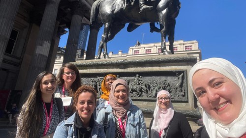 A group of even people standing by a large statue of a person on a horse in front of a city centre art gallery